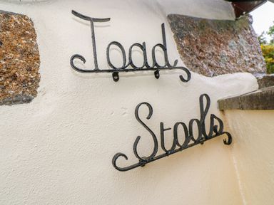 Decorative black metal signs reading Toad and Stools on a white wall with stone accents at Toadstools in Rame Cross near Penryn