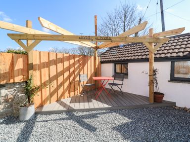 A small outdoor seating area with a wooden pergola a red table and two chairs at Toadstools in Rame Cross near Penryn