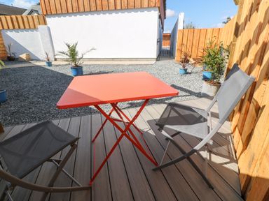 A small outdoor patio with a red square table and two gray chairs surrounded by wooden fencing and potted plants at Toadstools in Rame Cross near Penryn