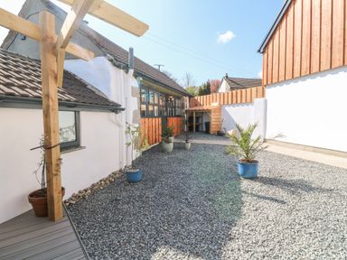 An outdoor courtyard with gravel ground and potted plants next to a white building with wooden accents at Toadstools in Rame Cross near Penryn
