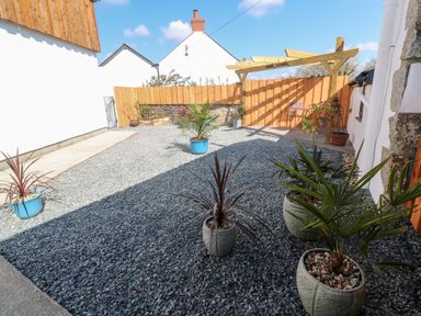 An outdoor patio area with gravel ground several potted plants a wooden pergola and fence at Toadstools in Rame Cross near Penryn