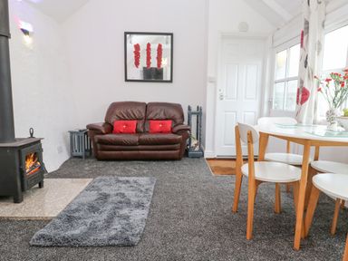 A sitting area with a brown leather sofa and a dining table with white chairs at Toadstools in Rame Cross near Penryn