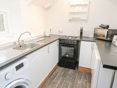 A kitchen with a washing machine sink stove kettle microwave toaster and shelves at Toadstools in Rame Cross near Penryn