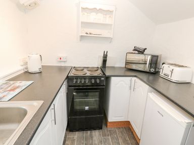 A kitchen with a black stove a white kettle a microwave a toaster and white cabinets at Toadstools in Rame Cross near Penryn
