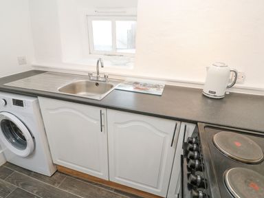 A kitchen countertop with a sink washing machine electric stove and kettle at Toadstools in Rame Cross near Penryn