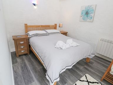 A bedroom with a wooden bed and side tables a painting and a radiator at Toadstools in Rame Cross near Penryn