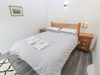 A bedroom with a wooden bed with pillows and a duvet two bedside tables a lamp and a framed picture on the wall at Toadstools Rame Cross near Penryn