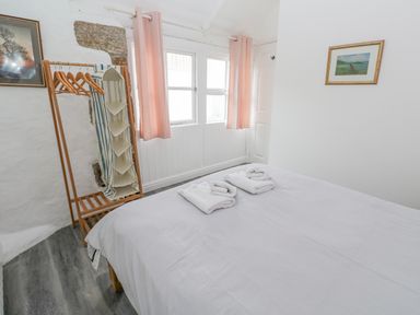 A bedroom with a bed and folded towels near a window with pink curtains at Toadstools in Rame Cross near Penryn