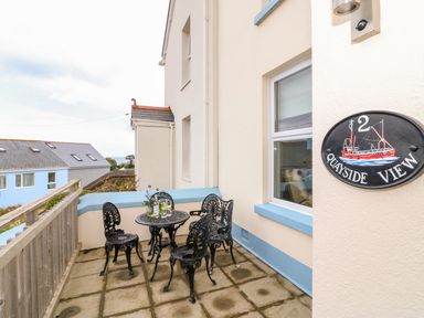 An outdoor patio with a black metal table and four chairs next to a cream building with blue trim at Quayside View in Brixham