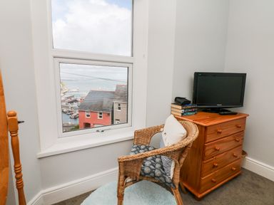 A corner of a room with a wicker chair and wooden dresser with a small television and books on top at Quayside View in Brixham