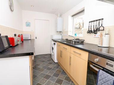 A kitchen with wooden cabinets black countertops a washing machine a drying rack kitchen utensils and appliances at Quayside View in Brixham