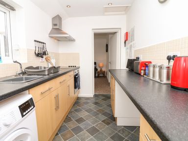 A kitchen with wooden cabinets a washing machine and red appliances at Quayside View in Brixham