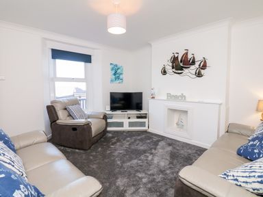 A living room with two sofas a recliner chair a television and a decorative wall hanging at Quayside View in Brixham