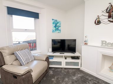 A corner of a living room with a recliner chair a television on a white stand and nautical decorations at Quayside View in Brixham
