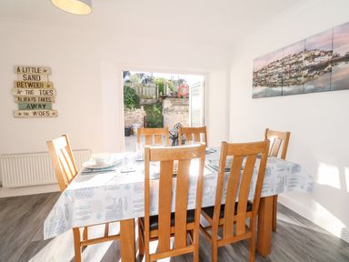 A dining room with a wooden table and six chairs set with dishes and glasses at Quayside View in Brixham