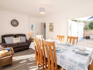 A dining area with a set table and wooden chairs next to a brown couch and an open door leading outside at Quayside View in Brixham