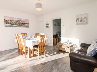 A dining area with a wooden table and six chairs set with plates and glasses and a brown leather sofa with pillows at Quayside View in Brixham