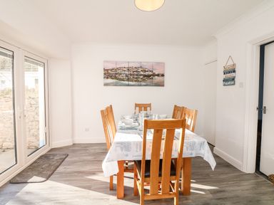 A dining room with a wooden table and six chairs set for a meal near glass doors with a wall picture and decorative sign at Quayside View in Brixham