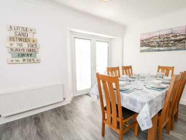 A dining room with a wooden table and six chairs set with plates and glasses at Quayside View in Brixham