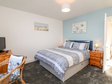 A bedroom with a bed two wooden nightstands a wicker chair and a TV at Quayside View in Brixham
