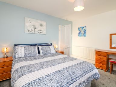 A bedroom with a double bed with patterned bedding two bedside tables with lamps a desk with a mirror and a chair at Quayside View in Brixham