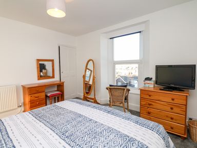 A bedroom with a bed near a window a wooden dresser with a TV and a wooden desk with a mirror at Quayside View in Brixham