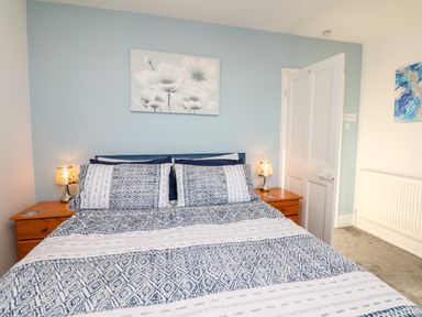 A bedroom with a bed with patterned bedding flanked by two wooden nightstands with lamps and floral wall art at Quayside View in Brixham