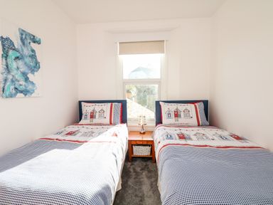 A bedroom with two single beds separated by a wooden nightstand with a lamp and a window behind them at Quayside View in Brixham