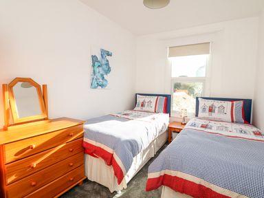 A bedroom with two single beds a wooden dresser with a mirror and a window at Quayside View in Brixham