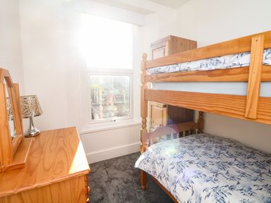 A bedroom with bunk beds a wooden dresser with a lamp and mirror and a window at Quayside View in Brixham