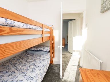 A bedroom with wooden bunk beds with patterned bedding a partially open door and a wooden dresser at Quayside View in Brixham