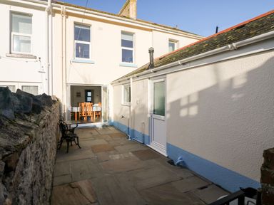 An outdoor patio with stone flooring benches and an open door showing a dining area at Quayside View in Brixham