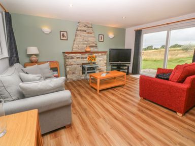A living room with grey and red sofas a stone fireplace and a television near sliding glass doors at 64 Waterside in Lanivet