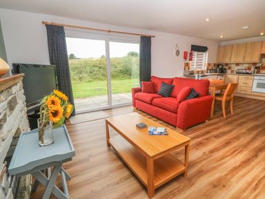 A living room with a red sofa wooden coffee table and television next to a kitchen and sliding glass doors at 64 Waterside in Lanivet