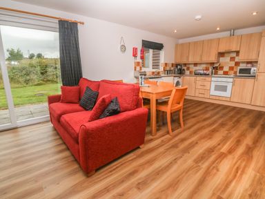 A kitchen and dining area with wooden cabinets a red sofa and sliding glass door at 64 Waterside in Lanivet