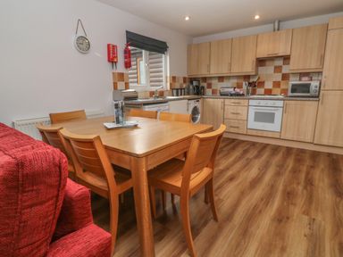 A kitchen with wooden cabinets, a dining table with six chairs, a window, and a red sofa at 64 Waterside in Lanivet