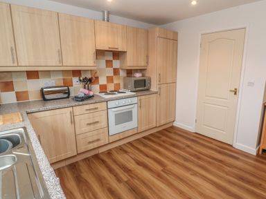 A kitchen with wooden cabinets an electric stove microwave toaster and sink at 64 Waterside in Lanivet