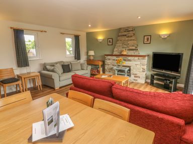 A living room with a stone fireplace television wooden tables chairs and sofas at 64 Waterside in Lanivet