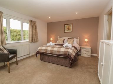 A bedroom with a double bed two nightstands lamps a chair and windows at 64 Waterside in Lanivet