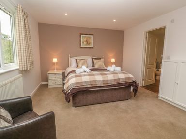 A bedroom with a bed and nightstands with lamps by a window and an armchair at 64 Waterside in Lanivet