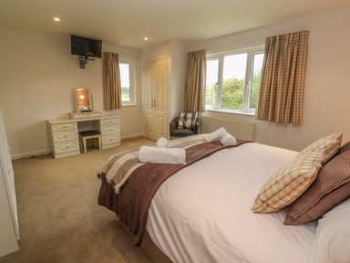 A bedroom with a bed with pillows and towels a dressing table a chair and windows with curtains at 64 Waterside in Lanivet