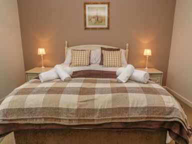 A bedroom with a bed with checkered blankets and pillows two bedside tables with lamps and a framed picture on the wall at 64 Waterside in Lanivet