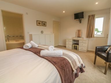 A bedroom with a bed with folded towels a dressing table a black chair a wall mounted tv and an en suite bathroom at 64 Waterside in Lanivet