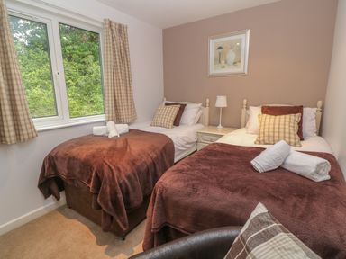 A bedroom with two single beds with brown blankets and plaid cushions next to a window at 64 Waterside in Lanivet