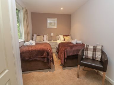 A bedroom with two single beds brown blankets and cushions a bedside table with a lamp and a chair with a pillow at 64 Waterside in Lanivet