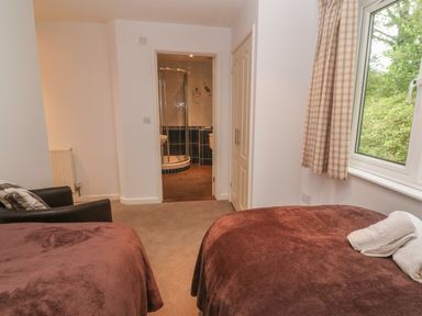 A bedroom with two beds brown blankets a window with checked curtains and an en suite bathroom at 64 Waterside in Lanivet