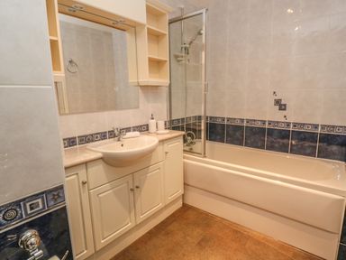 A bathroom with a sink, cabinet, bathtub with shower screen, and tiled walls at 64 Waterside in Lanivet