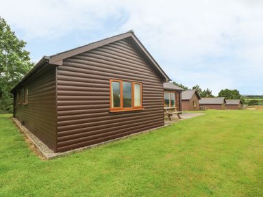 A row of brown wooden cabins with picnic tables on a grassy field at 64 Waterside in Lanivet