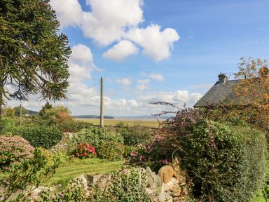 A garden with flowering plants and stone wall near a house with a sloped roof at Westmorland Cottage in Grange-Over-Sands