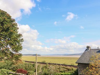 A landscape view with a tree and a house roof overlooking fields and a body of water at Westmorland Cottage in Grange-Over-Sands